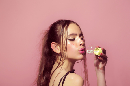 Bubble blower in hand of fashion model. Woman play with soap balloon. Girl with glamour makeup and hair. Fun and joy. Beauty and fashion.の写真素材