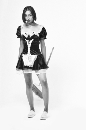 girl with pretty face in sexy maid costume with lace apron posing with sweep broom isolated on white background, black and whiteの写真素材