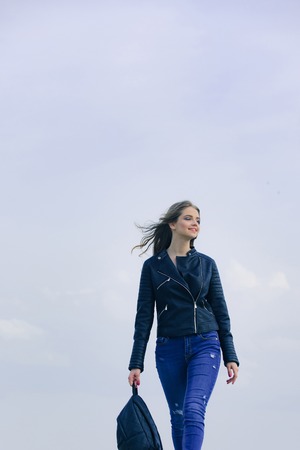 Girl in leather jacket with backpack. Woman with long hair. Sexy woman outdoor. Beauty and fashion. Fashion model on blue sky.の写真素材