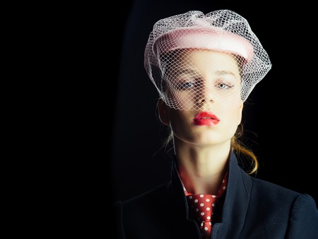 Girl in tie with red dots on neck. Lady posing on black background. Fashion and accessories. Retro or vintage style concept. Woman wearing pink hat with veil, copy spaceの写真素材