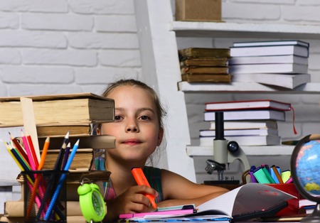 Kid and school supplies on white brick background. Back to school concept. Girl sits at desk with...
