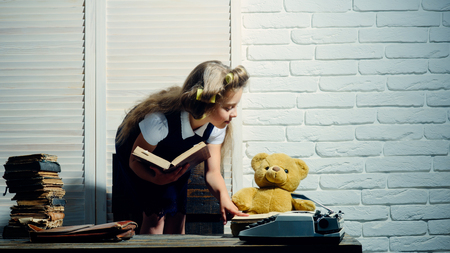 child or small girl with curler in hair read book with briefcase and retro typewriter on table in secretary or business cabinetの写真素材