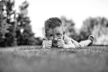 baby boy in shirt and eyeglasses on happy smiling face laying on grass summer day outdoor on natural background, black and whiteの写真素材