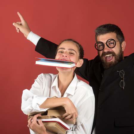 Education and back to school concept. Teacher and schoolgirl with happy faces on terracotta background. Girl and bearded man with glasses. Teenager and tutor hold pile of books and one in teethの写真素材