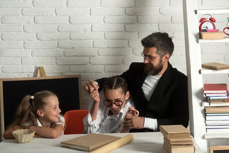 Kid, elder sister and their father with happy faces. Girls and bearded man sit at desk and have fun. Home schooling and back to school concept. Teacher and schoolgirls on classroom backgroundの写真素材