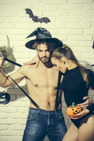 Halloween celebration and party concept. Man in witch hat with muscular torso. Girl holding pumpkin. Woman with long hair in black body suit. Couple in love hugging on white brick wall.の写真素材