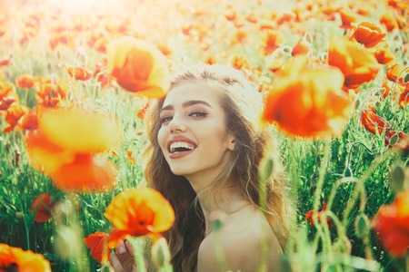 girl with long curly hair hold flower in field of red poppy seed with green stem on natural background, summer, spring, drug and love intoxication, opiumの写真素材