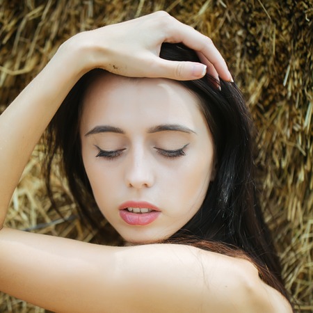 Girl with brunette hair posing in hay. Woman with closed eyes on cute face. Model with bare shoulders. Summer vacation concept. Leisure and relaxing on nature.の写真素材