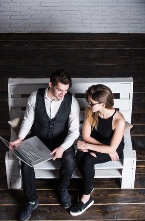 Woman in glasses. Studying and working concept. Students using computer. Guy and girl sitting on wooden bench. Man with laptop.の写真素材