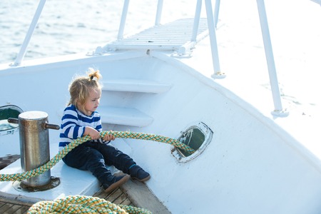 Travel and summer vacations. Little child sitting and berthing rope on white boat. Boy kid playing with rope on yacht. Baby care and childhood. Yachting and sailing concept.の写真素材