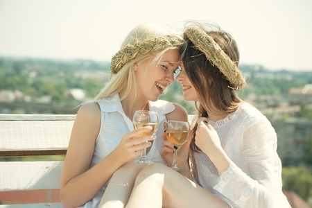 Girls smiling with champagne glasses outdoors. Happy girlfriends on bench on mountain landscape. Summer vacation, holidays and celebration. Wine tasting concept. Women drinking alcohol on sunny day.の写真素材