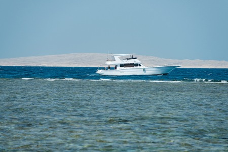 Yacht white beautiful marine vessel boat with engine and people on aboard traveling on summer vacations on background of blue ocean water and skyの写真素材