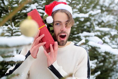Surprised macho in red santa hat on winter day. Season greetings and xmas gifts. Man holding present box in snow wood. Holidays celebration concept. Merry Christmas and happy new year.の写真素材