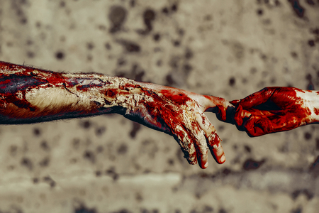 Halloween skin with red blood and bloody wounds. Connection and support. Holiday celebration concept. Female and male hands connecting. Two zombie touching fingers on concrete wall.の写真素材