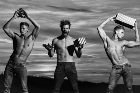 men or bodybuilders, handsome, young, male athlete people with sexy, muscular torso outdoors in sunset sky. guys holds present boxes for valentines or christmas holidays, black and whiteの写真素材
