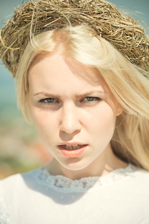 Girl with wreath on blond hair outdoors. Woman posing on blue sky. Summer vacation concept. Natural and healthy beauty. Model in white dress on sunny day.の写真素材