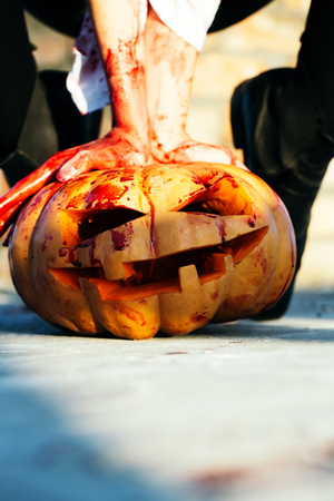 Halloween pumpkin with scary face, traditional autumn holiday symbol orange color with bloody male hands of zombie sunny outdoor, copy spaceの写真素材