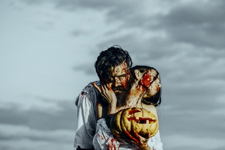 Halloween couple in love on grey sky. Man and woman bleeding with red blood. Hipster hugging girl with pumpkin. Vampires in bloody clothes. Halloween holiday celebration conceptの写真素材