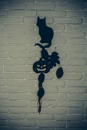 Halloween black cat, pumpkin and tree leaves silhouette paper cutouts on grey brick wall. Mystery and superstition concept. Holiday celebration symbolsの写真素材