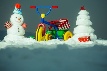Tricycle with present box on snowy background. Snowman and snow xmas tree on grey sky. Christmas and new year celebration. Festive surprise and gifts. Winter holidays conceptの写真素材