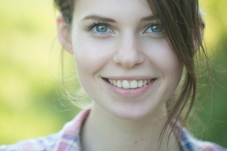 Happy woman smiling on blurred natural background. Health and beauty. Model in plaid shirt on sunny day. Summer vacation concept. Girl with brunette hair, hairstyle, outdoors.の写真素材