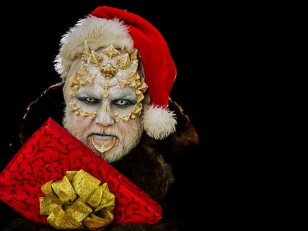 New year and christmas concept. Monster in santa hat and fur coat. Man with red present box. Elf with dragon skin and beard. Sorcerer face with white eyes and sharp thorns, copy spaceの写真素材