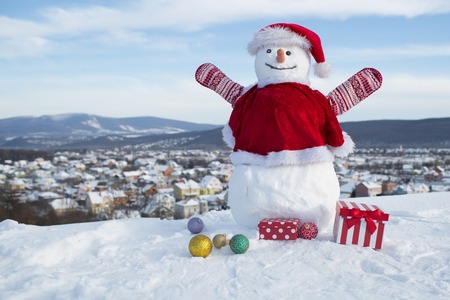 Happy holiday and celebration. Snowman in red santa claus hat. Christmas or xmas decoration. New year snowman from white snow with gift box. Winter activity and party.の写真素材