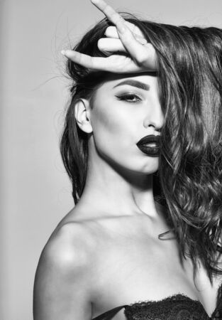 pretty woman or cute sexy girl with long curly brunette hair, has red lips, makeup on adorable face on grey backgroundの写真素材