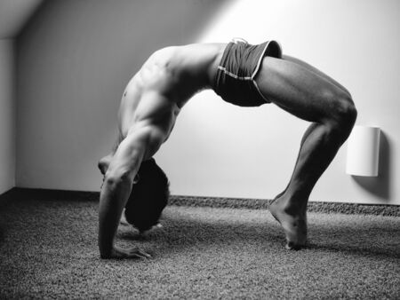 Yoga practice. Man doing bridge yoga pose with leg in room near window
