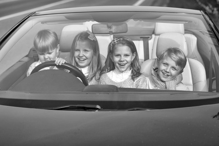 Cute four baby children friends of girls and boys people with at wheel pretends driving car as drivers on road outdoorの写真素材