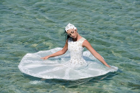 Fashion and beauty. Bride on sunny summer day on seascape. Girl sitting in sea water. Honeymoon travel concept. Woman in white wedding dress.の写真素材