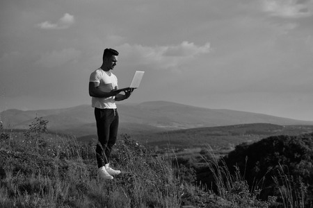 Young handsome man with muscular sexy body standing with laptop outdoor sunny day on blue sky backgroundの写真素材