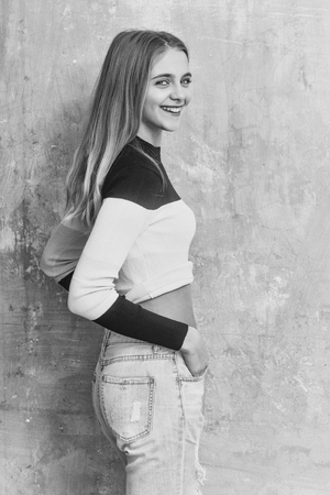 Pretty smiling girl or cute young woman with blond hair and adorable happy face in fashionable black white sweater on textured wall background, copy spaceの写真素材