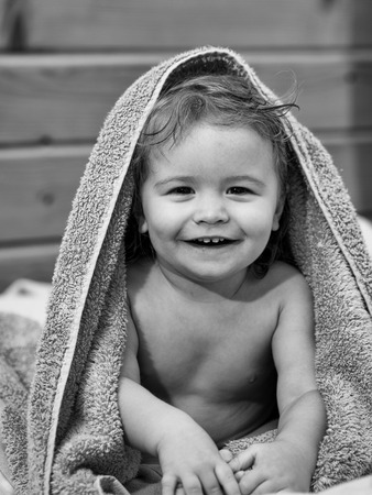Cute happy beautiful smiling playful child boy with wet hair sitting in hothouse bath yellow fluffy towel naked indoor on wooden background, vertical pictureの写真素材