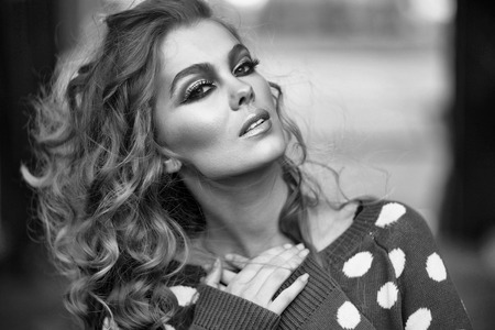 Pretty girl or beautiful woman with stylish makeup and long curly hair wearing blue polka dot sweater on blurred backgroundの写真素材