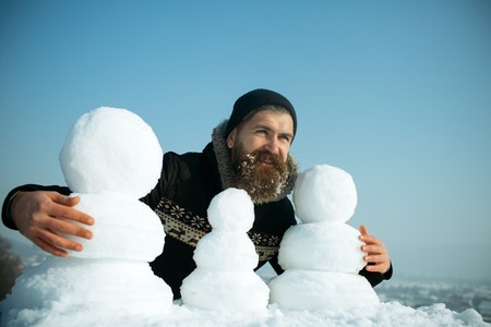 Santa claus hipster in coat and snowman. Snowman family made of white snow New year guy on blue sky with snow figure. Winter holiday vacation and xmas party celebration. Christmas man with long beard.の写真素材
