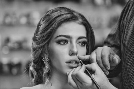 Guy stylist doing makeup beautiful woman in beauty salon with wavy hairstyleの写真素材