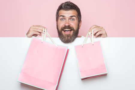 Christmas and birthday. Hipster with present package on pink background. Guy with happy face and gift pack. Man with long beard with pink shopping bag. Holiday celebration and black friday shopping.の写真素材