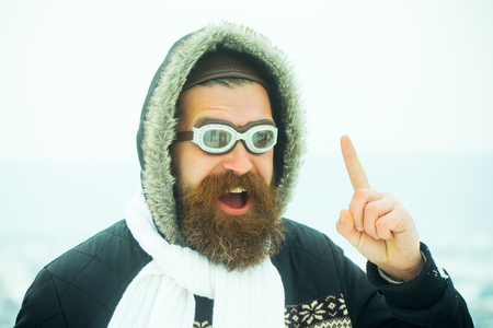 Winter holiday and vacation. Hipster in coat, glasses and hood. New year guy on blue sky with snow. Xmas party celebration. Christmas man with long beard.の写真素材