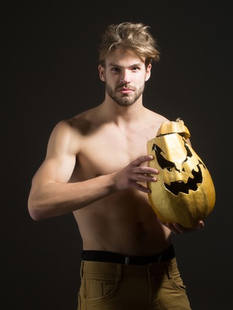 Halloween holidays celebration concept. Autumn and harvest season. Macho holding jack o lantern pumpkin. Man with muscular torso, biceps, triceps on black background. Trick or treat.の写真素材