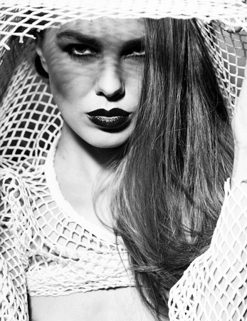 Pretty girl or sexy woman with beautiful red lips, stylish makeup, and long hair wearing beige fishnet shirt on light backgroundの写真素材