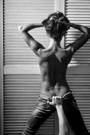 pretty woman or cute girl with sexy naked body and back standing in blue jeans with male hand at white wardrobe doorの写真素材