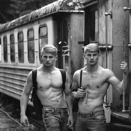 Handsome young guys with muscular body standing shirtless in pants with beautiful torso near blue old train railcarの写真素材