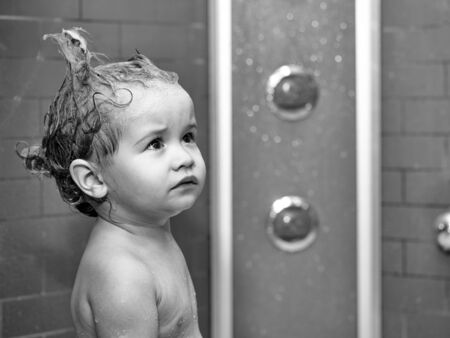 Cute happy smiling funny undressed boy child with blonde curly wet hair taking shower in bath with water indoor, horizontal pictureの写真素材
