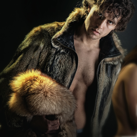 Man or macho posing in open fur coat of brown furry animal hides with bare torso on dark background. Fashion and clothing. Glamour and luxury lifestyle conceptの写真素材