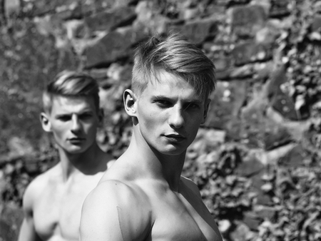 Muscular young twins with beautiful sexy body and bare torso standing outdoor on masonry wall background with vineの写真素材