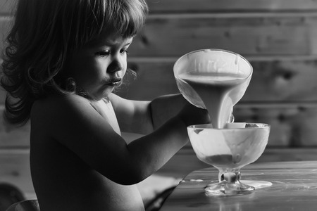 Small baby boy with blonde hair and cute face eating yoghurt from glass bowl toplessの写真素材