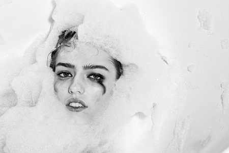 Closeup view portrait of one beautiful sensual sexy attractive young woman with wet bright makeup lying in bath tub with water and lots of white soap foam looking away copy space, horizontal pictureの写真素材