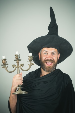 Halloween bearded man with happy face in black coat and witch hat hold candleの写真素材