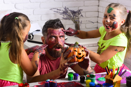 Halloween Kids or small girls with bearded man father hold pumpkin. Holiday and party celebration. \family with colorful paint. Art and color painting. Halloween children with happy face in paint.の写真素材